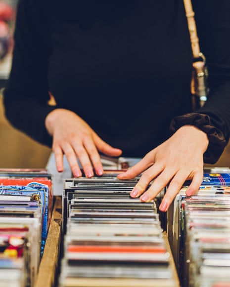 A young woman's hands browse rows of CDs in a shop, torso cropped out of frame
