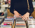 A young woman's hands browse rows of CDs in a shop, torso cropped out of frame
