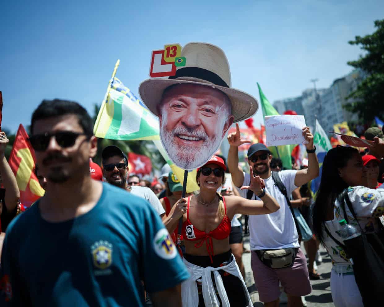 Supporters at a Lula rally, with a woman holding a large cutout of his smiling face.