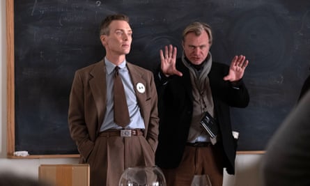 Two men. One is gesturing with his hand while another is standing with his hands in his pant pockets.