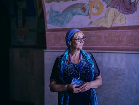 An older woman in a headscarf standing in front of a mural of a decapitated saint