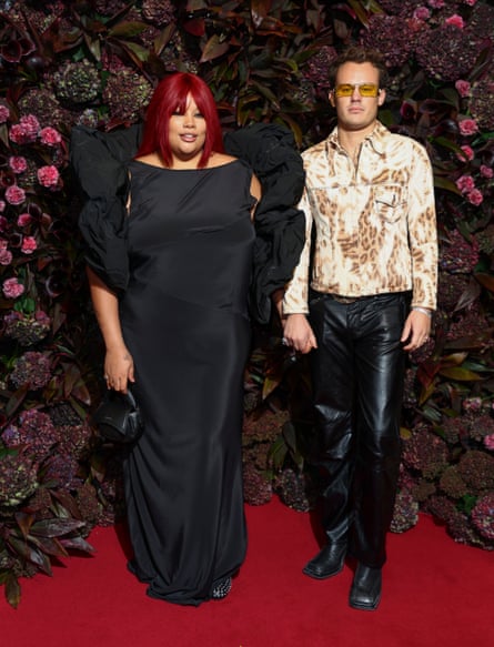 The couple pose against a floral backdrop, Shygirl wearing a long black dress and Smale in black leather trousers and an animal print jacket