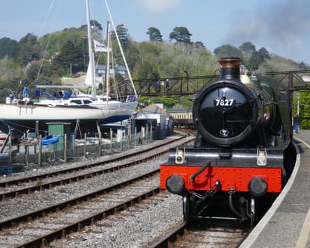 A steam engine and carriages in a station, with a boat in dry dock beside the track