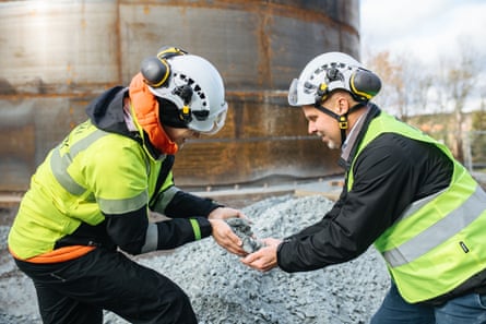 Two people in helmets and hi-vis jackets pass soapstone to each other at a facility