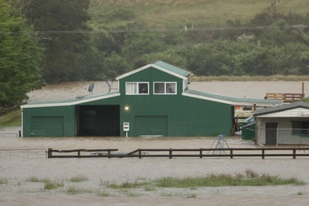 A person speaks on their phone as they look out of their window at the flood waters surrounding their property in Huapai, north-west of Auckland, on Tuesday