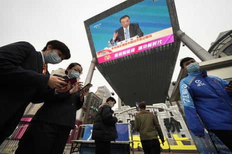 People walk past a large video screen at a shopping mall showing Chinese Premier Li Keqiang as he speaks during a press conference after the closing session of China’s National People’s Congress (NPC) in Beijing.