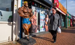 A woman holds her head and grimaces as she walks past a sculpture of a tanned semi-nude muscleman in Wellingborough