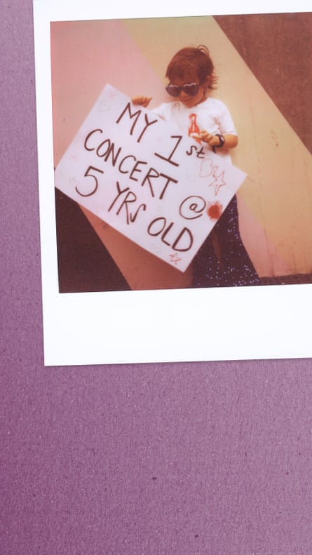 A chlid wearing sunglasses holding a sign that reads ‘My 1st Concert @ 5 yrs old’