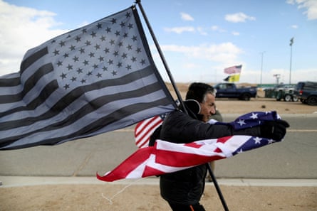 A man holds a black-and-white US flag as trucks gather in the background.