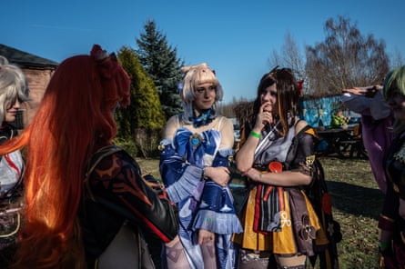 A group of people in colourful cosplay costumes stand outdoors on a sunny day, chatting together.