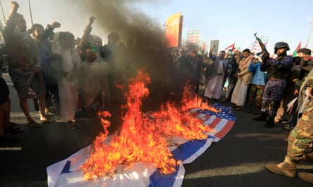 حشد من الرجال يحملون البنادق ويرفعون قبضاتهم في الهواء ويحيطون بالأعلام الإسرائيلية والأمريكية المشتعلة على الأرض خلال احتجاج في اليمن