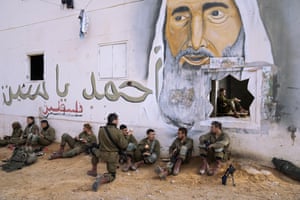 Israeli soldiers rest next to a mural depicting the late Hamas leader Sheikh Ahmad Yassin