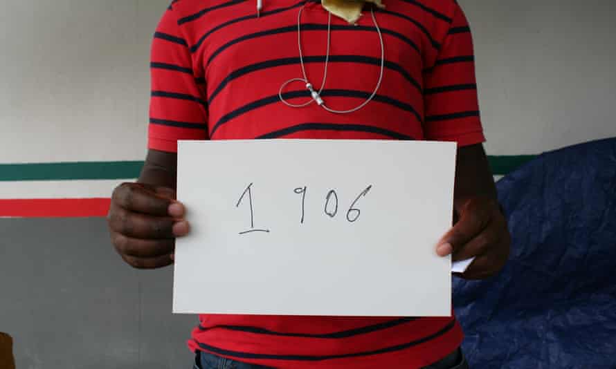 “Mike” from Douala, Cameroon, poses with his immigration number outside the Gateway International Bridge in Matamoros, Mexico.