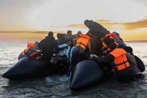 People wearing orange buoyancy aids try to climb on to an overloaded dinghy