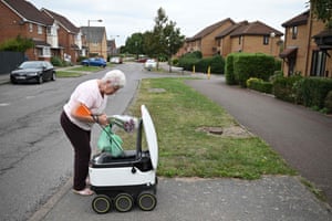 Milton Keynes, England: A resident picks up a delivery from an autonomous robot delivering groceries from a nearby Co-op supermarket