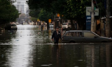 A man walks through a flooded street past a partially submerged car