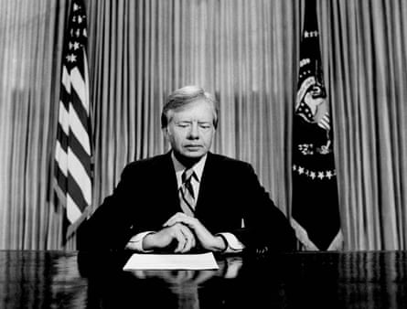Jimmy Carter sits astatine his table looking pensive successful beforehand of a US flag.