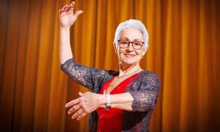Zaragoza-Martinez, with short hair, smiles in front of a curtain with one hand up and the other out as if embracing a dance partner
