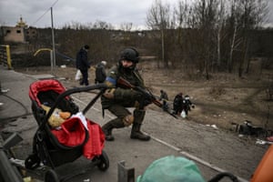 An Ukrainian serviceman takes cover as people evacuate the city of Irpin.