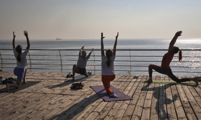 Women practice yoga on a beach by the Black Sea as the ship Navi-Star carrying a load of corn, leaves the port in Odesa, Ukraine, Friday, Aug. 5, 2022. Ukraine is a major global grain supplier but the war had blocked most exports, so the July 22 deal aimed to ease food security around the globe. World food prices have been soaring in a crisis blamed on the war, supply chain problems and COVID-19. (AP Photo/Nina Lyashonok)