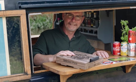 Paul Partridge, smiling and passing a pizza in a box through the hatch of his narrowboat