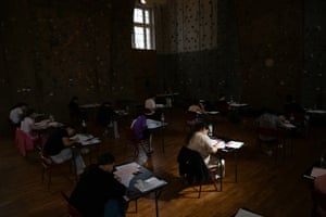 Sunlight falls on one student writing at desk surrounded by others in the shadows around her