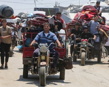 People drive cargo tricycles stacked high with belongings, as others walk alongside carrying possessions