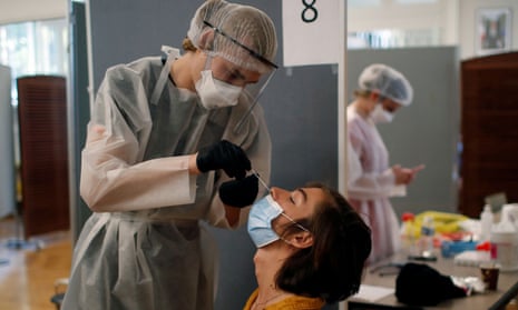 A health worker, wearing a protective suit and a face mask, administers a nasal swab to a patient at a testing site in Paris.