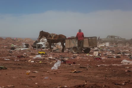 A horse and cart stand in the middle of a flat area covered in dirt and rubbish.