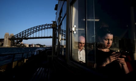 A commuter uses her mobile phone as a Circular Quay to Cockatoo Island ferry passes under the Sydney Harbour Bridge