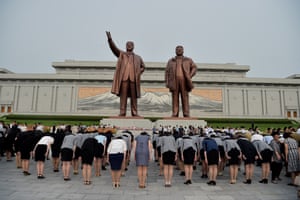 People bow in front of two huge bronze statues