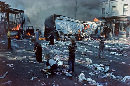 Children playing among debris from hijacked burning vehicles after riots in west Belfast, August 1976.