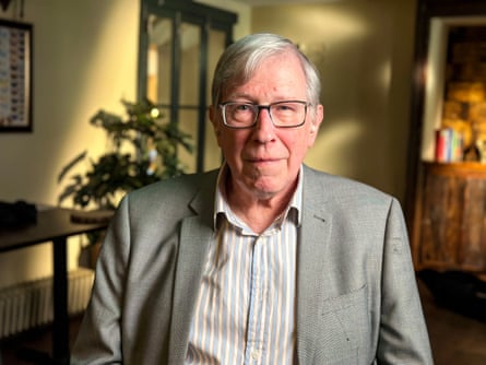 A man with grey hair wearing a light grey suit jacket and glasses