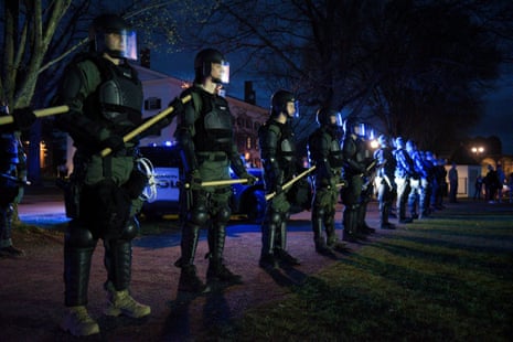 Police line up with black armor, helmets and clubs at the ready.