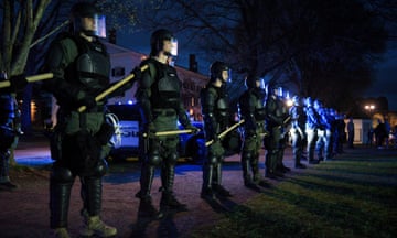 Police line up with black armor, helmets and clubs at the ready.