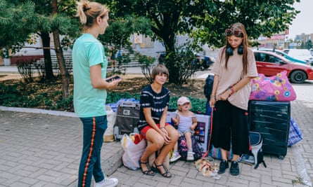 A woman and child stand, while two other children sit on bags