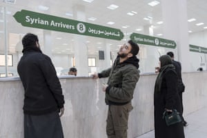 Akram Aljnidi looks up at the sign reading "Syrian arrivers" while standing at the counter, with his mother beside him