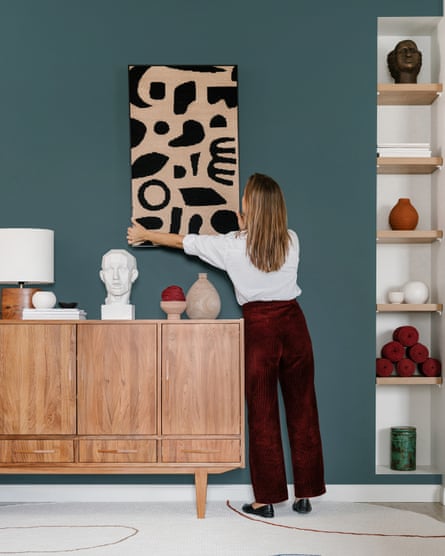 Back view of unrecognizable female designer hanging picture with abstract ornament on painted wall while working on creative interior design of modern apartment