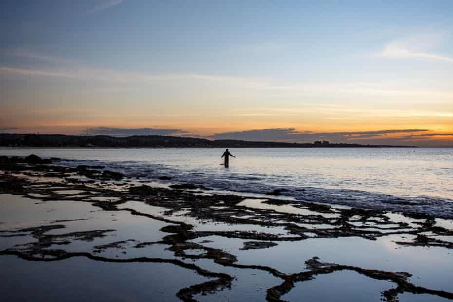 A man fishes on the beach at sunset