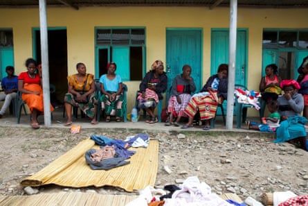 Woman and a young boy sit on chairs outside a building, with some possessions laid on the ground in front of them
