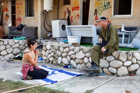 A woman prepares to write a message on an Israel flag in front of a building damaged during the 7 October Hamas attack on kibbutz Kfar Aza in southern Israel.