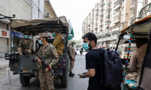 A resident wearing a protective mask walks past Pakistan Army soldiers on patrol to enforce coronavirus disease safety protocols in Karachi.