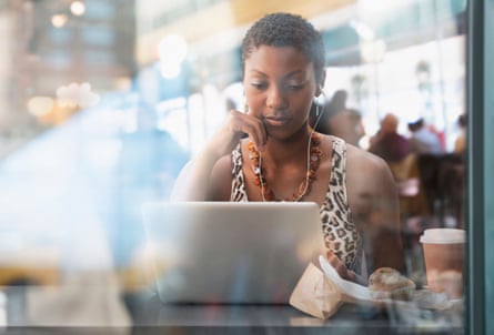 Woman using wired headphones and a laptop in a busy cafe.
