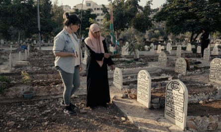 An older woman shows a younger woman a new gravestone in a flat graveyard