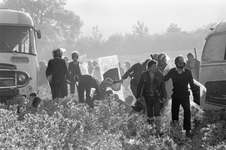 Police detain people as two buses brought to a halt sit among the crops.