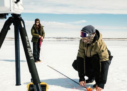 One person is squatting near a tripod and the other is standing holding a cable