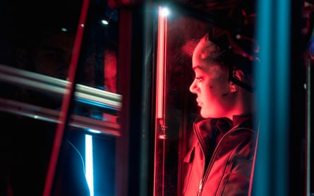 A woman with a red glow around her looking through bars at a glimpse of man’s face