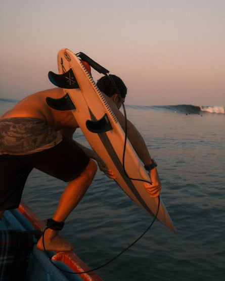 A surfer about to leap into the water from a boat carrying a board