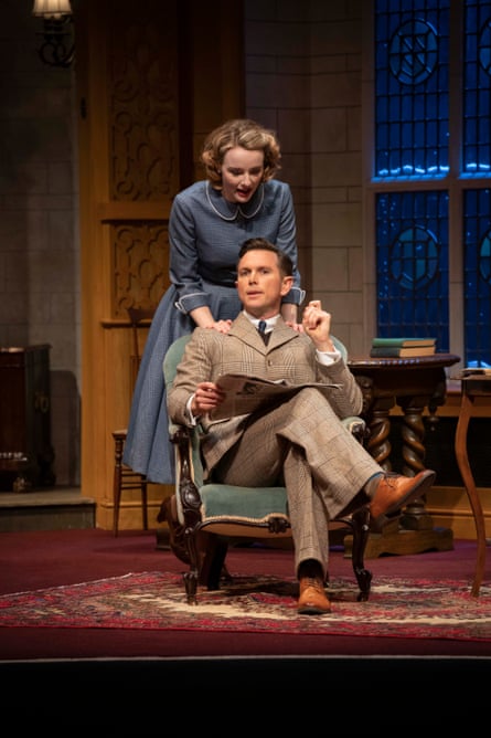Anna O’Byrne and Alex Rathgeber performing on stage in The Mousetrap. O'Byrne is standing behind Rathgeber who is sitting in a chair. She has her hands on his shoulders and he is reading a newspaper