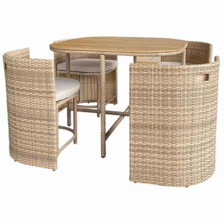 A garden table with wooden top is surrounded by 4 wicker like chairs with white cushions.